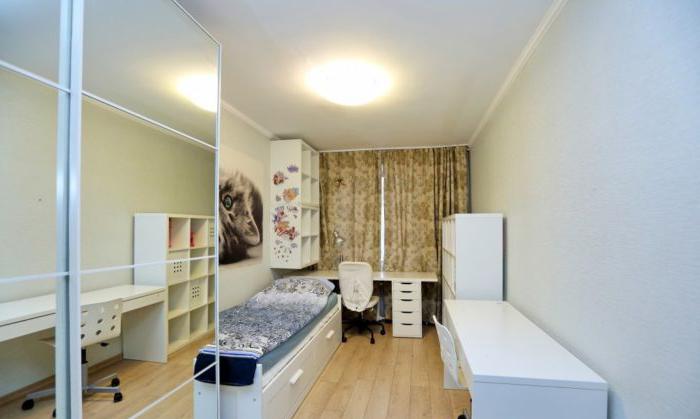 La stretta stanza di una ragazza adolescente con un'area di lavoro vicino alla finestra e un letto con cassetti