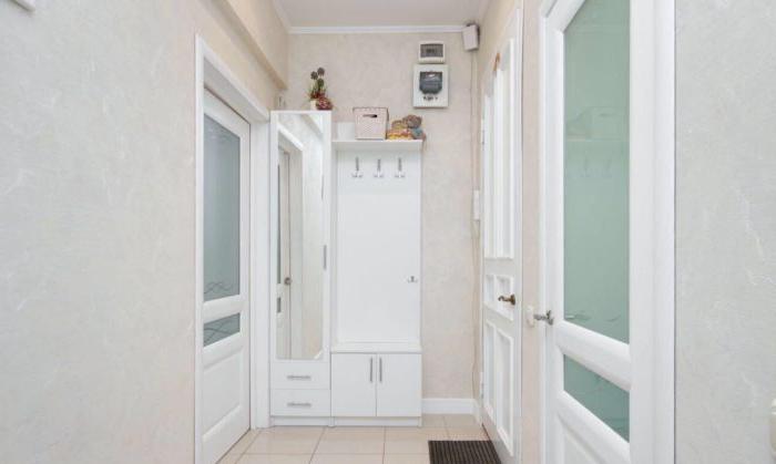 Piccolo armadio bianco nel corridoio con appendiabiti aperti, una panca e uno specchio